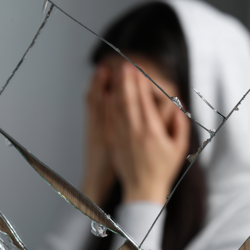 Broken Mirror as a common superstition. Image is of woman with face covered in front of a broken glass.